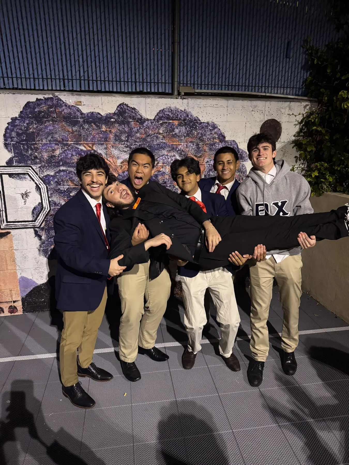 Brothers in suits and ties carrying a newly initiated brother in front of the house mural