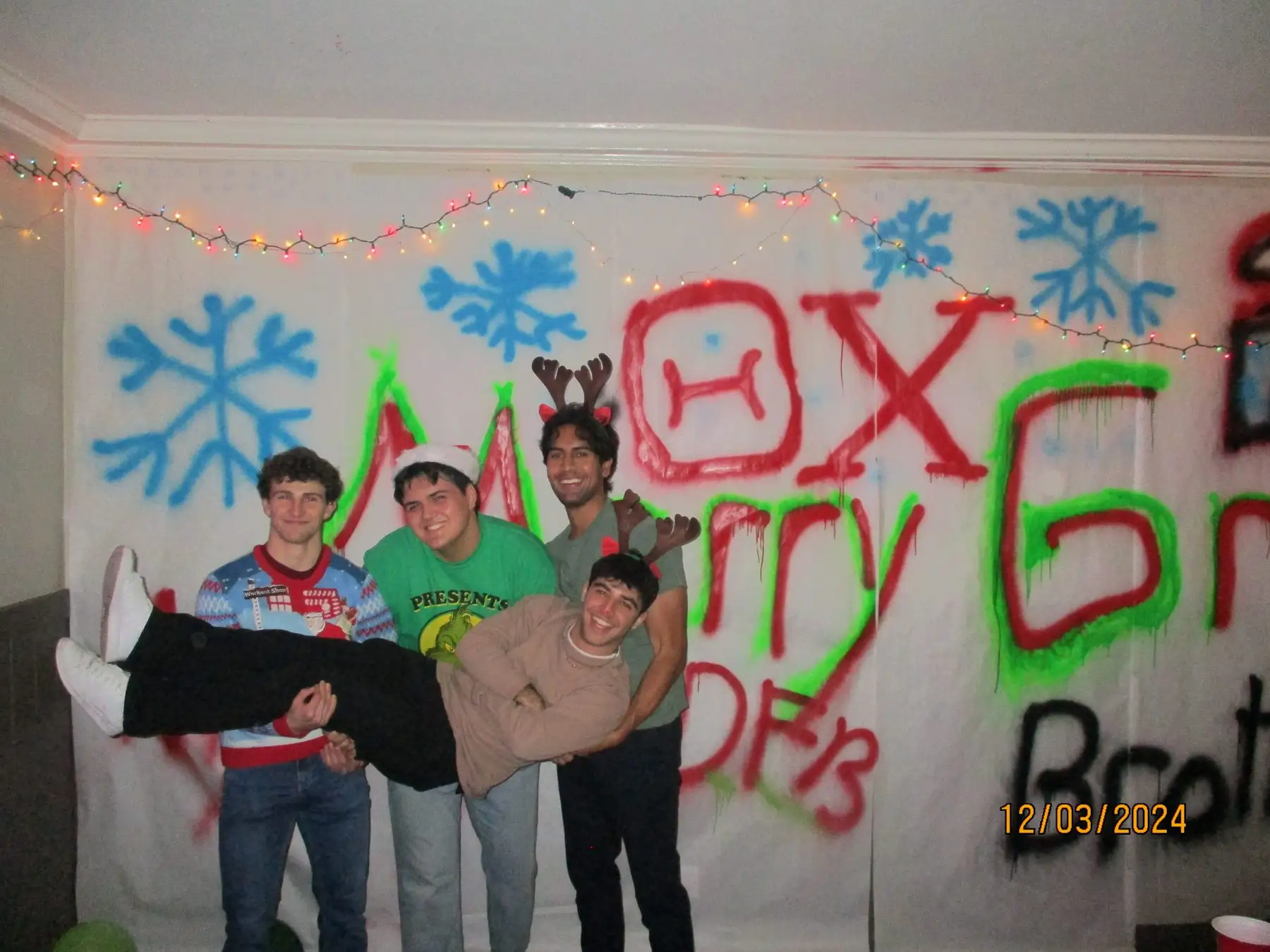 Brothers lifting a friend in front of the holiday photo wall