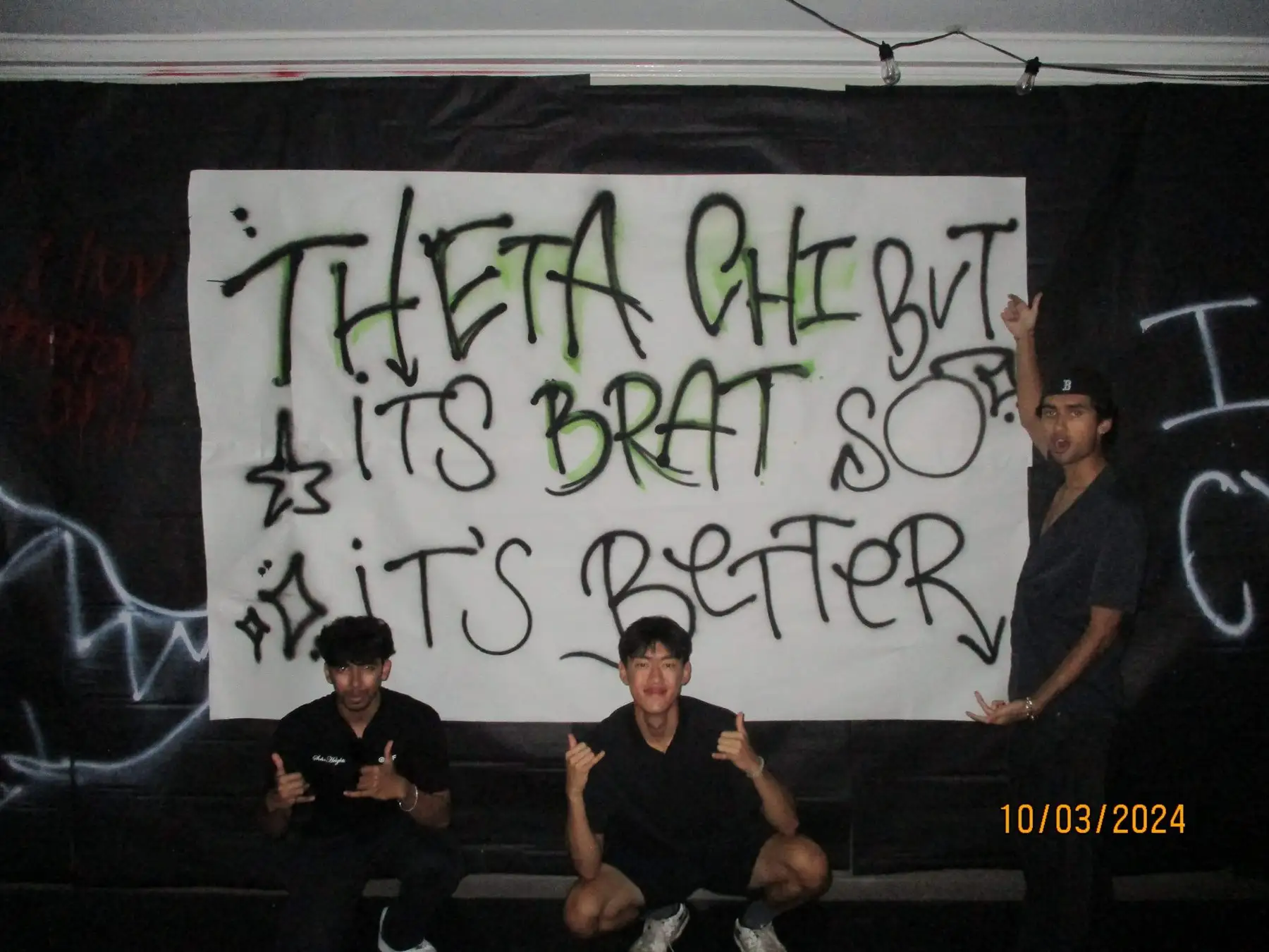 Three brothers posing in front of a hand-painted Theta Chi banner