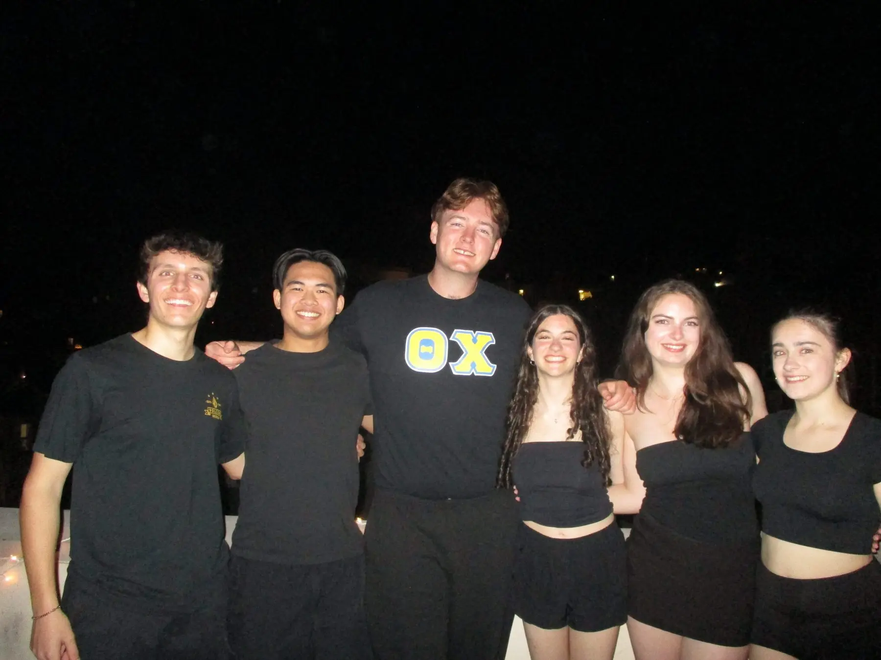 A brother in Theta Chi letters with five friends on the roof at night